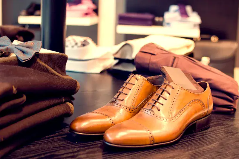 Brown leather dress shoes on a store table next to folded clothes