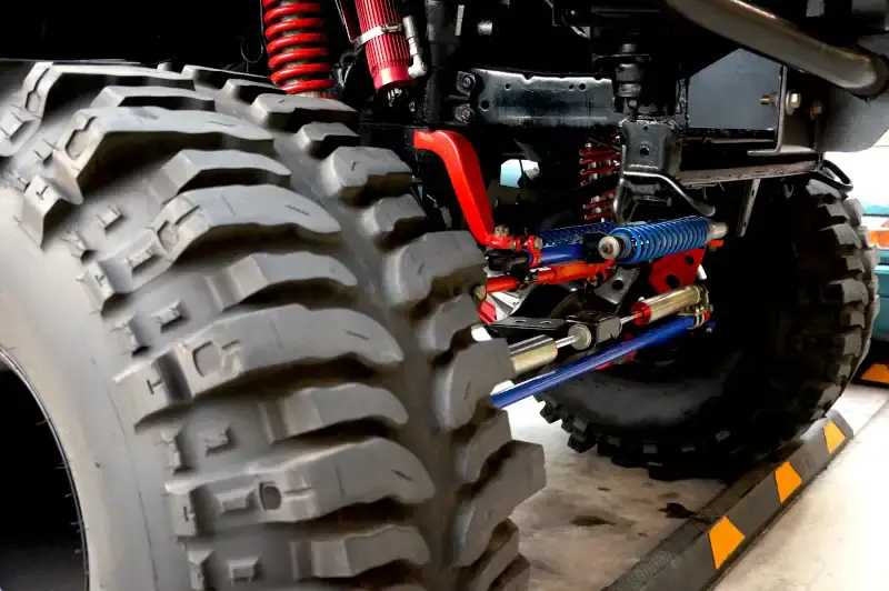 Off-road truck suspension with red coil-over shocks above a large mud tire