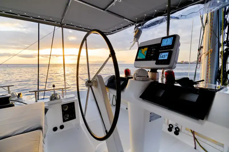 A sailboat’s helm with its wheel and navigation displays at sunset